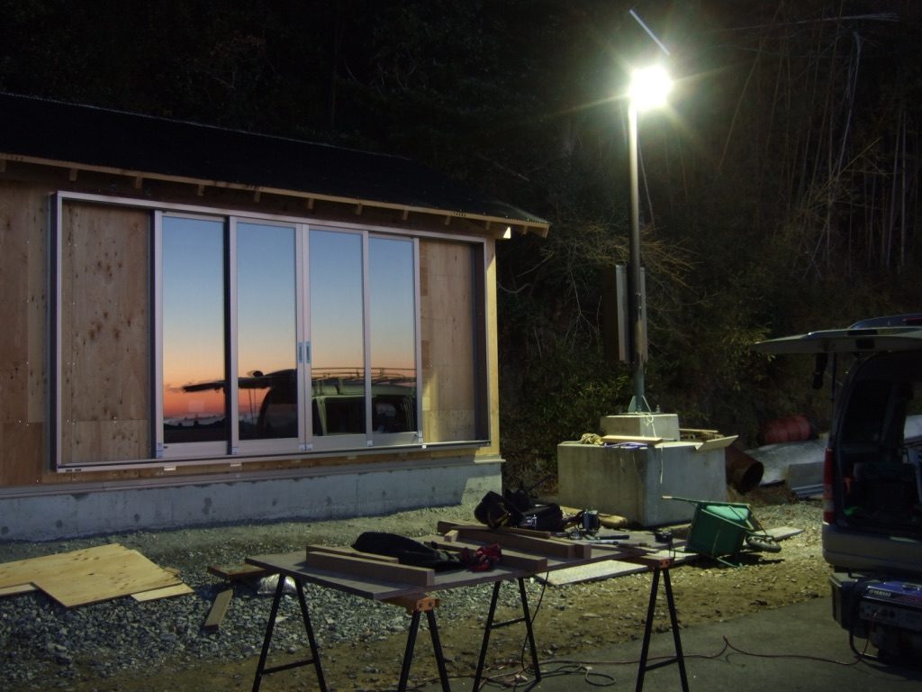 夕暮れの現場に灯りがともったタイニーハウスのサッシ